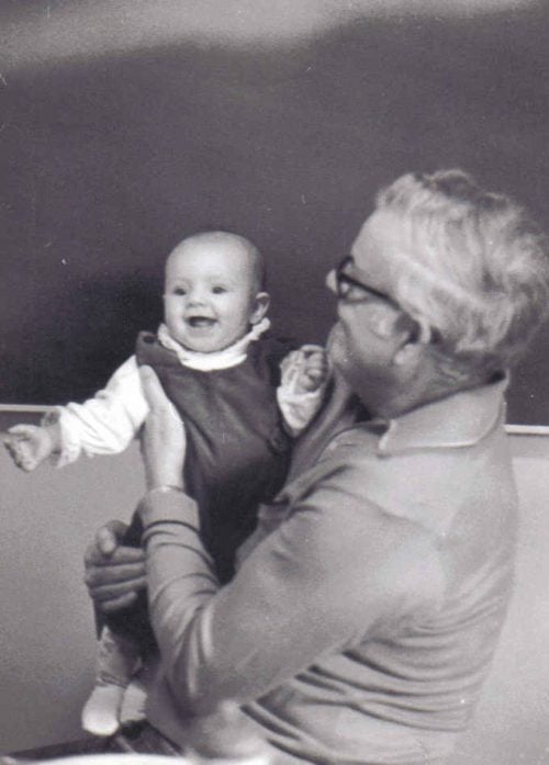 greyscale image of elderly man in glasses holding a baby in a jumper