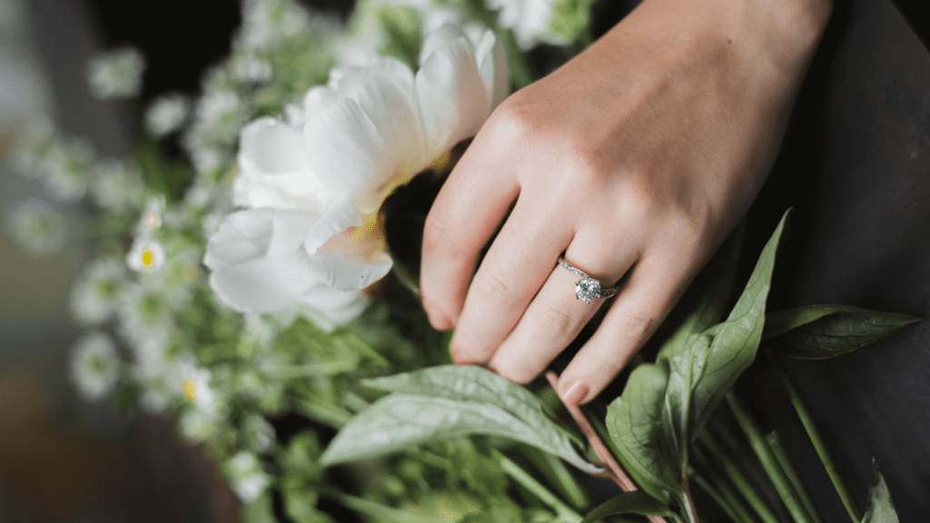 Hand with floral engagement ring holding a white flower